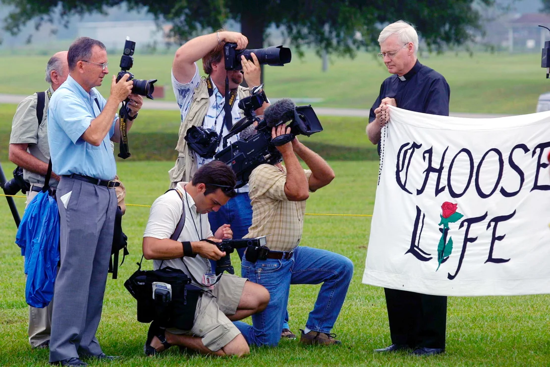 Miembros de la prensa fotografían al sacerdote Fred Ruse mientras sostiene una pancarta con el mensaje “Choose Life” antes de la ejecución de Aileen Wuornos en Florida.